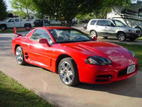 1999 Mitsubishi 3000GT - A red 1999 Mitsubishi 3000GT is parked on a driveway, with other vehicles in the background.