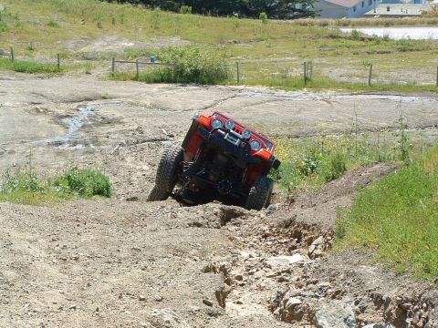 1999 Jeep Grand Cherokee - Red Jeep Wrangler navigating a challenging off-road course with steep inclines and rocky terrain.