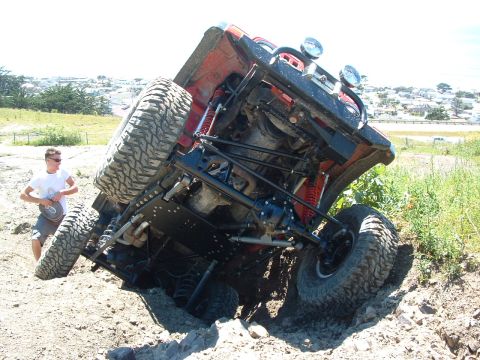 1999 Jeep Grand Cherokee - A person watches an off-road vehicle that has tipped onto its side in the dirt.