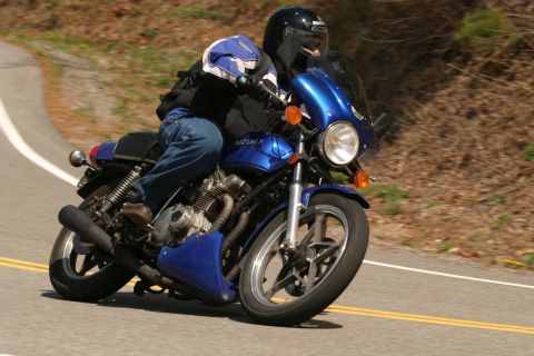 1985 Ford LTD Crown Victoria - A rider leans into a turn on a blue motorcycle on a sunny day.