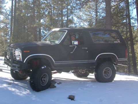 1984 Ford Bronco - A modified Ford Bronco sits in a snowy, wooded area with its driver inside.