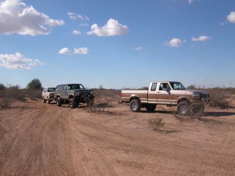 1992 Ford F-150 - Two trucks and a Bronco drive off-road under a partly cloudy sky.