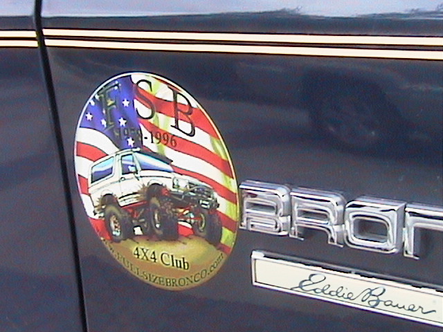 Close-up of a dark blue vehicle's side showing a "Bronco" emblem and an oval sticker with a lifted Bronco graphic