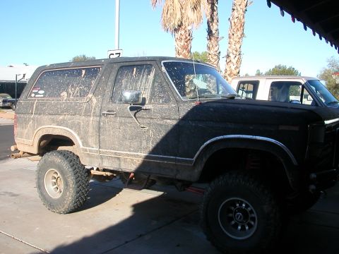 1984 Ford Bronco - This 1980s Ford Bronco is covered in mud, suggesting recent off-road use. Another vehicle is partially visible behind it.
