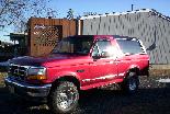1995 Ford Bronco - This red 1995 Ford Bronco is parked in front of a building on a sunny day.
