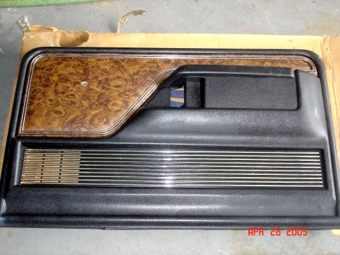 1979 Ford Bronco - A car door panel with faux wood grain trim and horizontal chrome accents is shown.