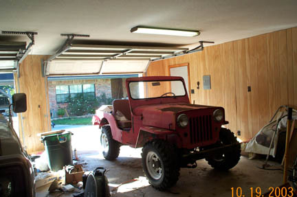 1954 Jeep Wrangler - A red 1954 Jeep CJ-5 is parked inside a garage with the doors open.