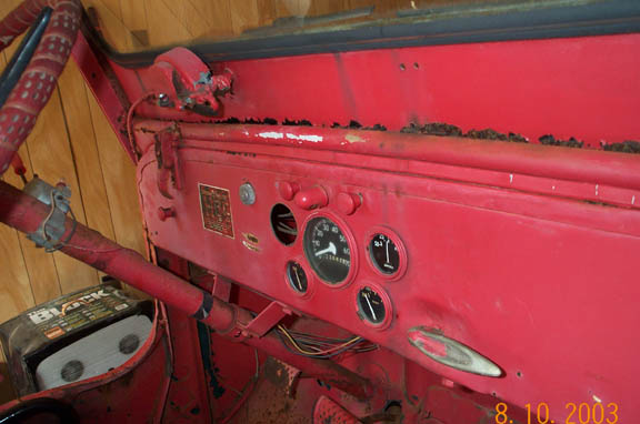 Red vintage Jeep dashboard with round gauges, rust, and exposed wiring.