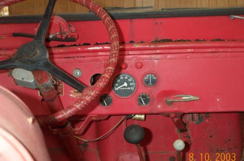 1954 Jeep Wrangler - The interior of a vintage vehicle shows a red dashboard with a steering wheel and various gauges.