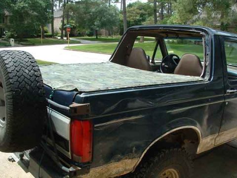 1993 Ford Bronco - Rear view of a 1993 Ford Bronco, a spare tire on the back and a camouflage soft top covering the bed.