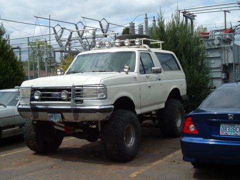 1989 Ford Bronco - White 1989 Ford Bronco lifted with off-road lights and bull bar, parked next to a blue sedan.