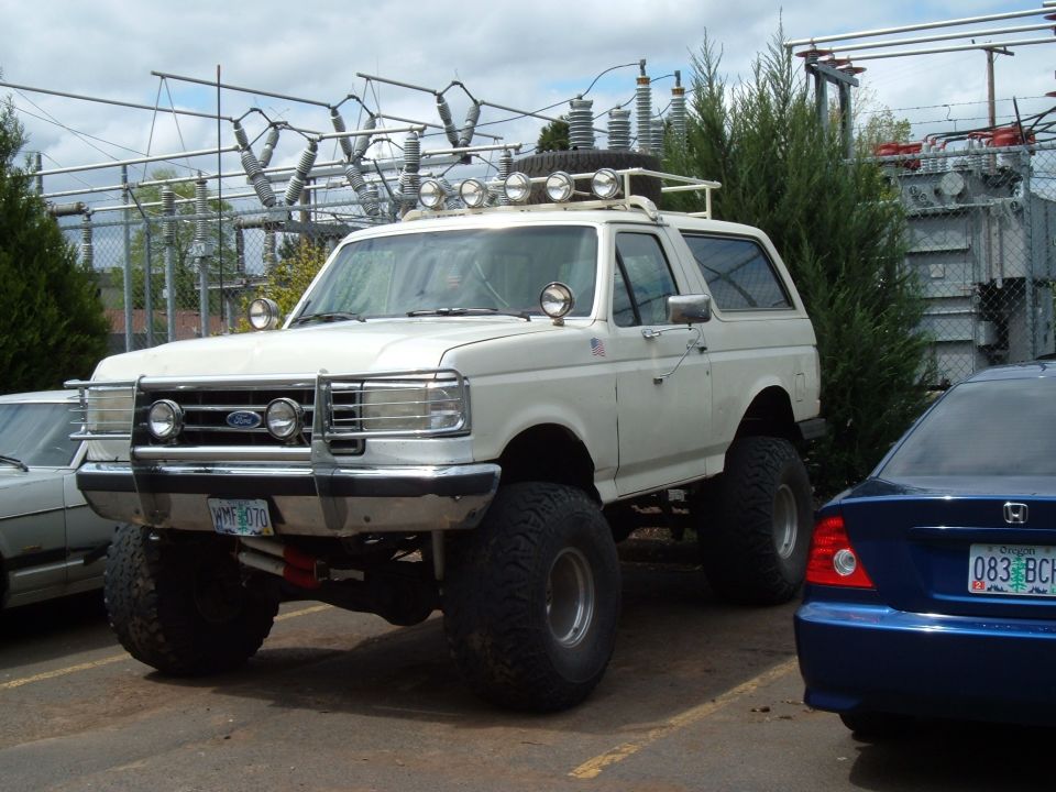 Lifted white Ford Bronco with roof light bar and grille guard parked by a substation