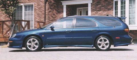 1999 Ford Taurus - A blue Ford Taurus station wagon shown in profile (driver's side) with chrome multi-spoke alloy wheels, lower body side skirts, and a small…