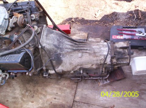 1985 Ford Bronco - An engine and transmission assembly sits on wooden planks, with tools visible in the background. The date 04/28/2005 is watermarked on the…