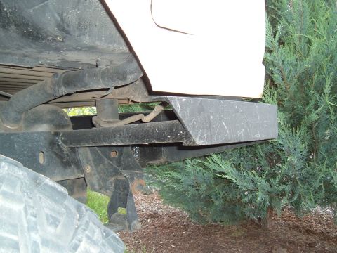 1989 Ford Bronco - Close-up view of the rear undercarriage and bumper assembly of a vehicle, with foliage in the background.