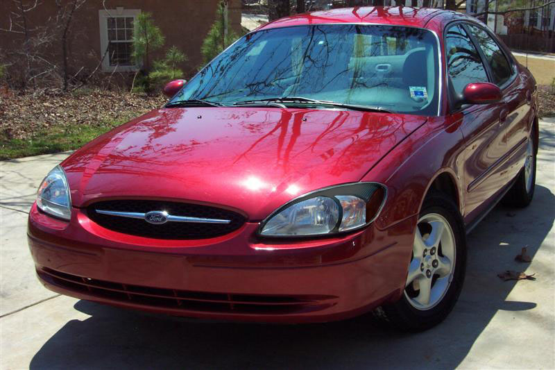 Red sedan, front 3/4 view, parked outdoors. The car has a chrome grille with a Ford logo and alloy wheels