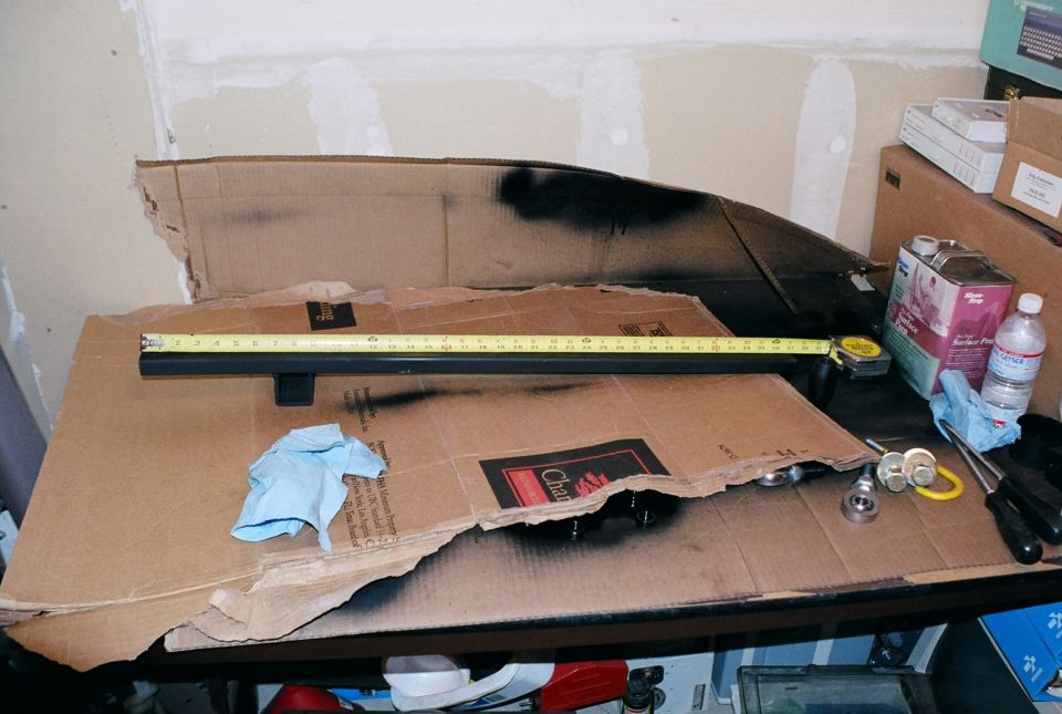 Black tube part with a tape measure laid on cardboard over a workbench