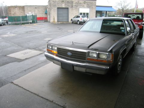 1991 Ford LTD Crown Victoria - A dark 1990 Ford Crown Victoria is parked on wet pavement next to a red Jeep, with a commercial building in the background.