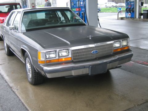 1991 Ford LTD Crown Victoria - A gray 1988 Ford LTD Crown Victoria is parked at a gas pump, with a red vehicle visible to its left.