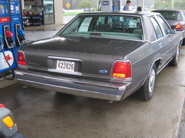 Gray Ford Crown Victoria sedan from rear 3/4 at a gas station pump island