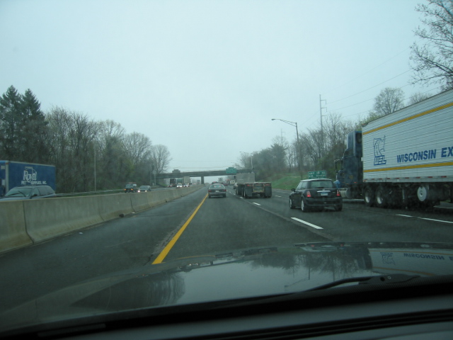 Highway scene with multiple vehicles including a semi-trailer truck with "WISCONSIN EX" text, a black Mini Cooper, and other cars