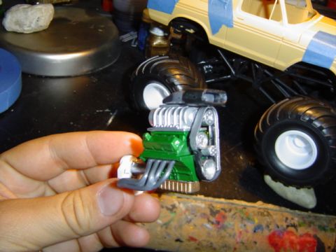 1979 Ford Bronco - A person is assembling a model monster truck, holding the engine while the chassis is visible.