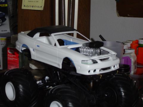 1979 Ford Bronco - A model car with a supercharger sits atop a monster truck chassis, surrounded by hobby supplies.