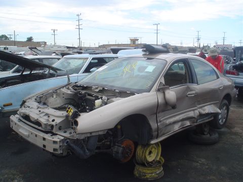 1993 Ford Taurus - Junkyard sedan with extensive damage to the front and side, missing wheels and hood.
