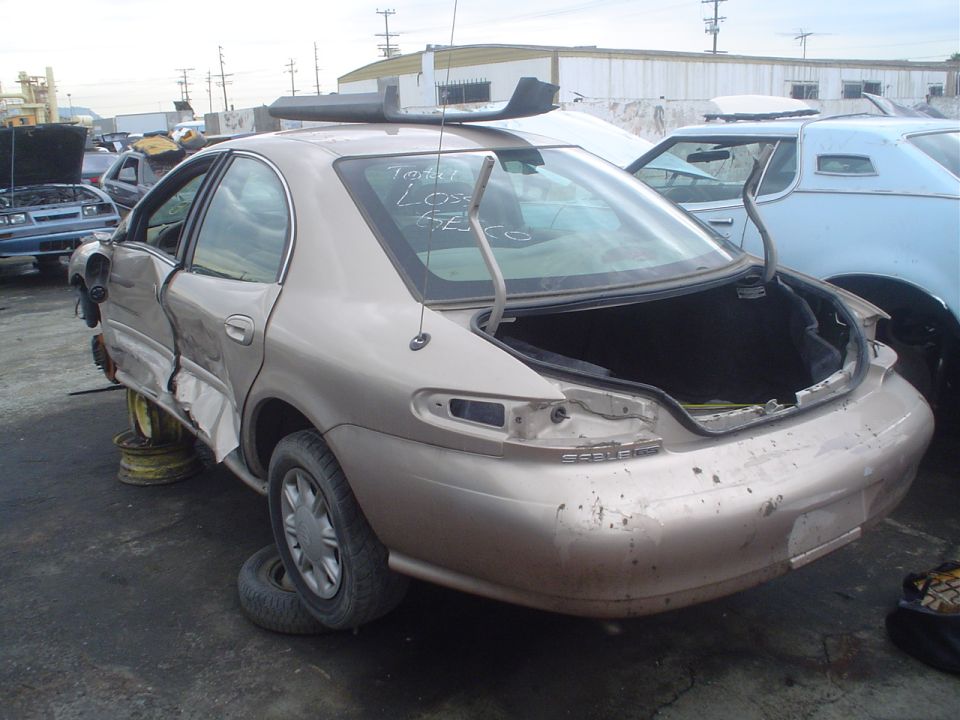 tan sedan with trunk open, rear quarter panel damaged, in junkyard