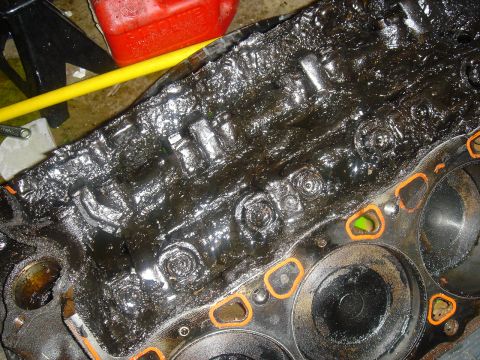 1986 Ford Mustang - Close-up of a heavily soiled engine block, showing internal components coated in dark, viscous sludge.