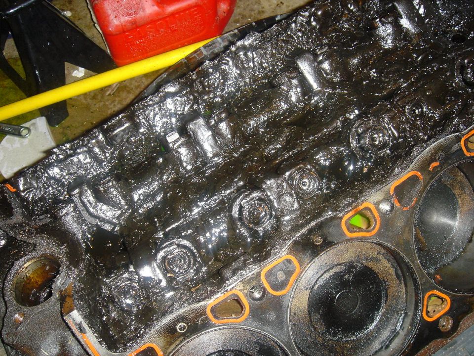 Engine block covered in thick, black sludge with orange gasket material visible