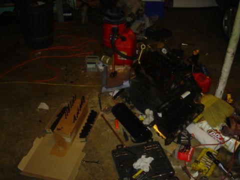 1986 Ford Mustang - A collection of engine components and tools are spread across a garage floor, suggesting a project in progress.