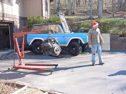1972 Ford Bronco - A blue 1972 Ford Bronco is parked outside a garage with its engine removed and suspended by an engine hoist.
