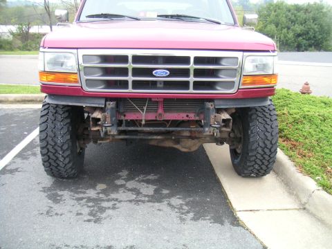 1994 Ford Bronco - Front view of a red Ford Bronco with a lifted suspension and off-road tires.