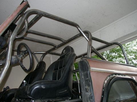 1995 Ford Bronco - The interior of a vehicle shows a custom roll cage structure installed over the seats and steering wheel.