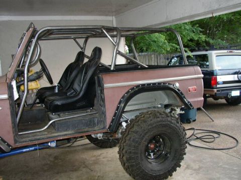 1995 Ford Bronco - A modified Ford Bronco with a roll cage sits in a garage, with another Bronco visible in the background.