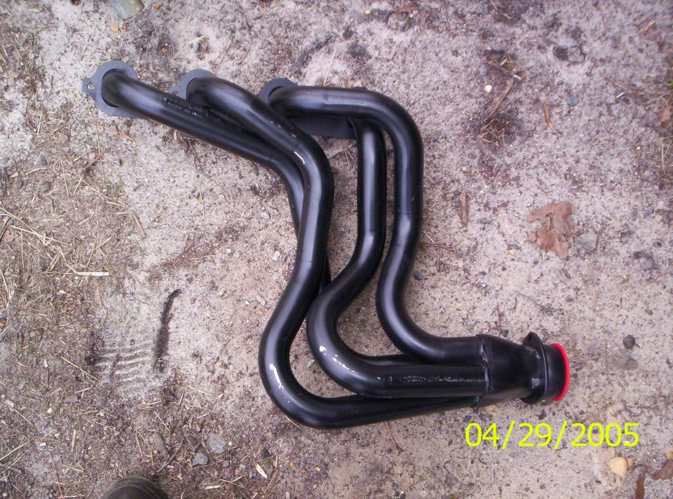 Black exhaust headers with red cap on one end, lying on dirt ground