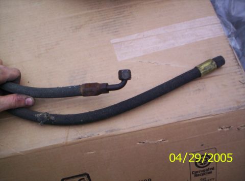 1985 Ford Bronco - A close-up view of an automotive hose with metal connectors, placed on a cardboard surface.