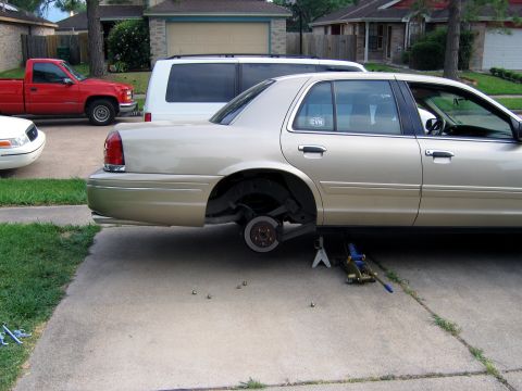 2000 Ford Crown Victoria - A gold 2000 Ford Crown Victoria is parked on a driveway with its rear wheel removed and supported by jack stands.