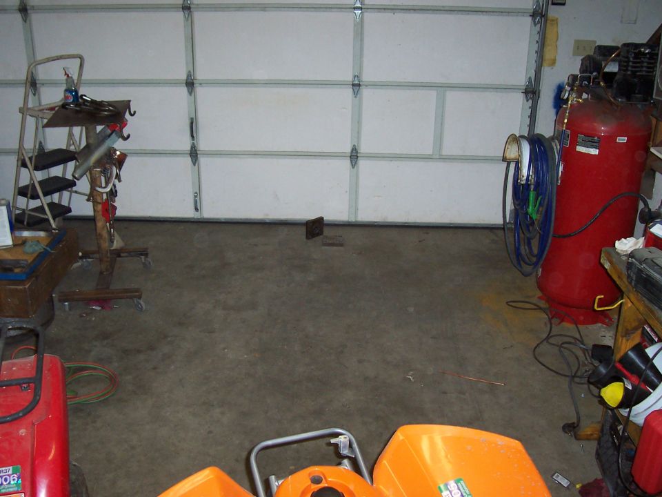 Garage with a large red air compressor, ladder, and parts of an orange ATV. A closed garage door is in the background