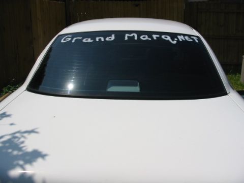 1997 Ford Crown Victoria - The rear of a white sedan shows "Grand Marq.NET" written on the tinted window.