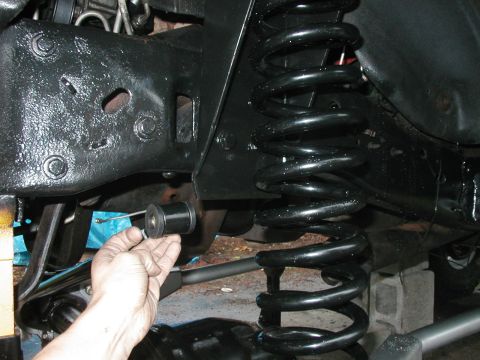 1994 Ford Bronco - A hand holds a black suspension bushing near the coil spring and frame of a vehicle.