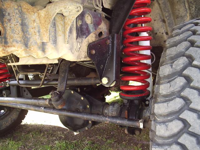 Undercarriage of lifted Bronco with red coil spring, white shock, and mud tire