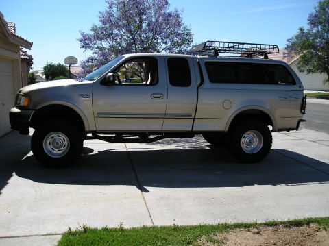 1999 Ford F-150 - Side view of a lifted 1999 Ford F-150 pickup truck equipped with a camper shell and roof rack.
