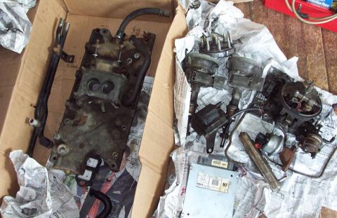 1985 Ford Crown Victoria LTD - Various engine components, including an intake manifold and distributors, are shown packed in a cardboard box.