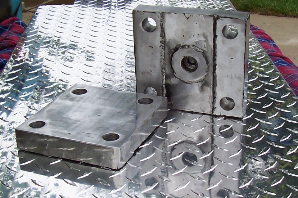 Two metal brackets with four bolt holes each, resting on a diamond plate surface