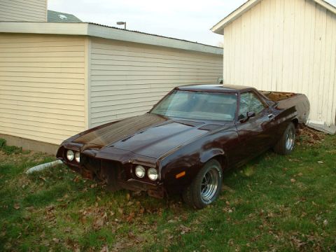 1972 Ford Ranchero - A 1972 Ford Ranchero sits in front of a building with its front end missing some parts.