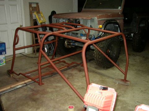 1995 Ford Bronco - A custom-built roll cage is positioned in front of a vintage Ford Bronco undergoing modifications.