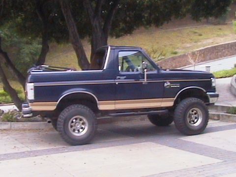 1991 Ford Bronco - A dark blue Ford Bronco with the soft top removed, shown in profile facing right, featuring tan lower body two-tone paint, a suspension lif…