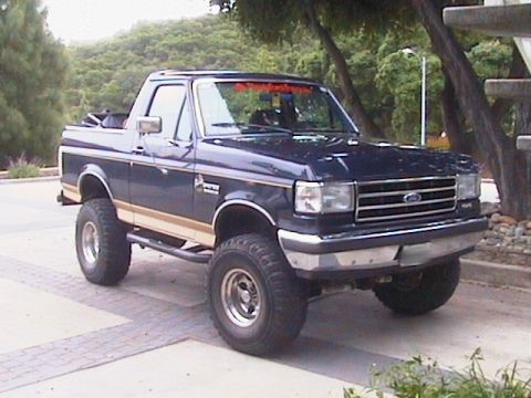 1991 Ford Bronco - Dark blue lifted Ford full-size Bronco with Eddie Bauer trim and chrome wheels, parked on pavement, front three-quarter view.